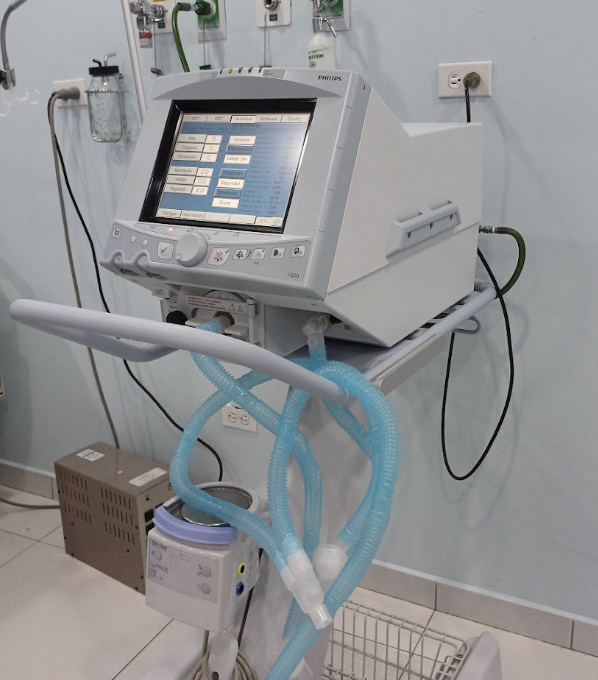Ventilador Philips con pantalla de control, circuito respiratorio y humidificador sobre soporte móvil